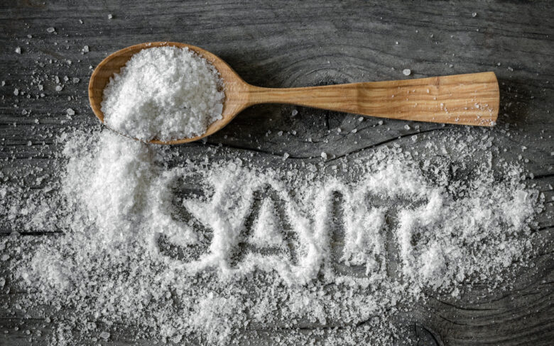 塩が乗った木のスプーンとグレーのテーブル上にばらまかれた塩、そこにSALTの文字を浮かび上がらせている
